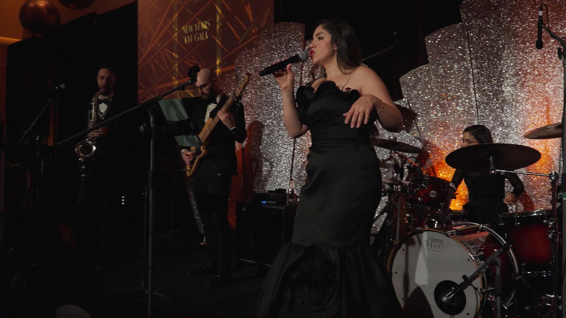 Vocalist in a black gown singing with a live band on a glittering stage at a year-end gala party