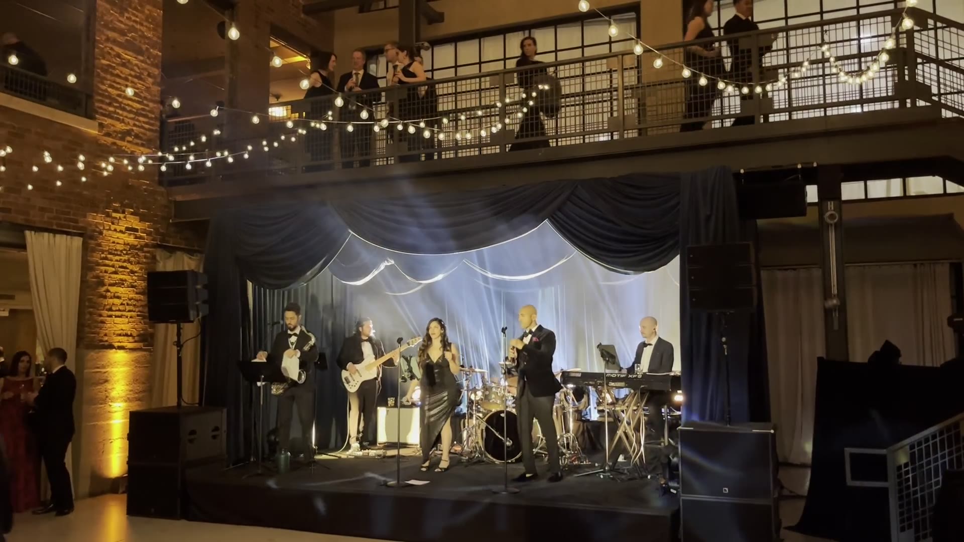 Live entertainment on a lit stage above an open dance floor at an evening event, with guests watching from a balcony